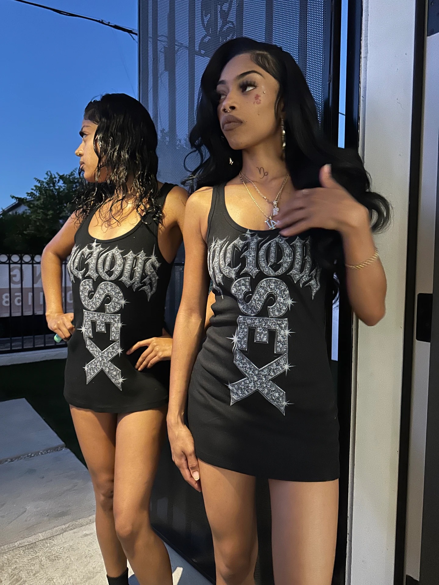 Two models wearing VICIOUS WORLD black statement tank tops at dusk